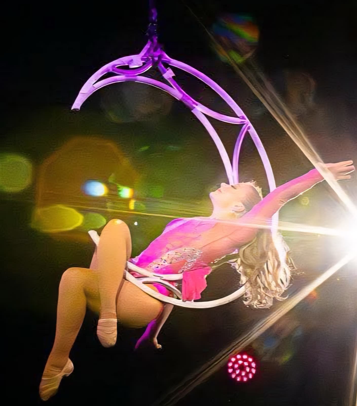 An aerialist reclining in a crescent-moon hoop high above the ring