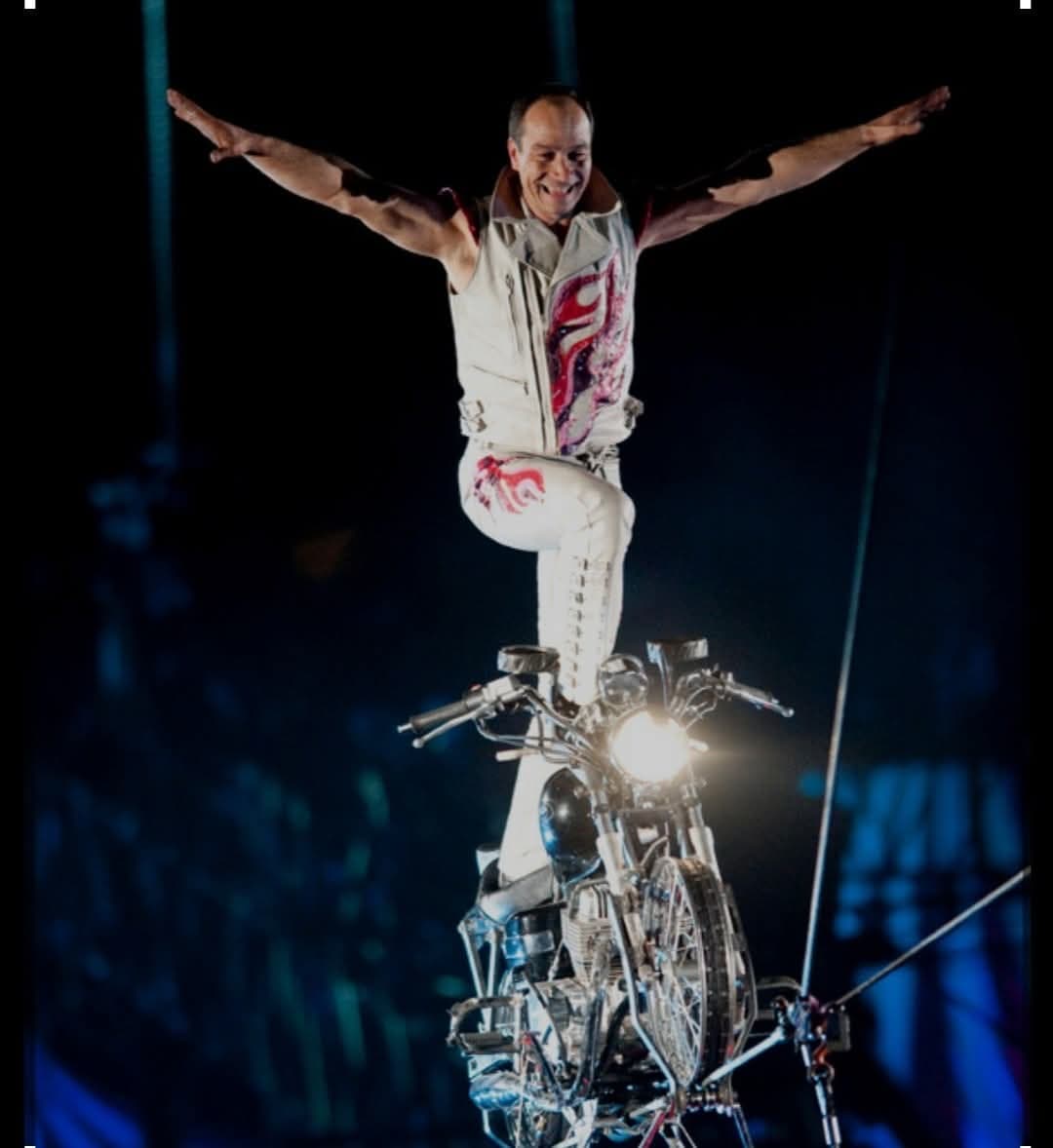 A rider standing on the seat of a motorcycle balanced on the high wire, arms outstretched