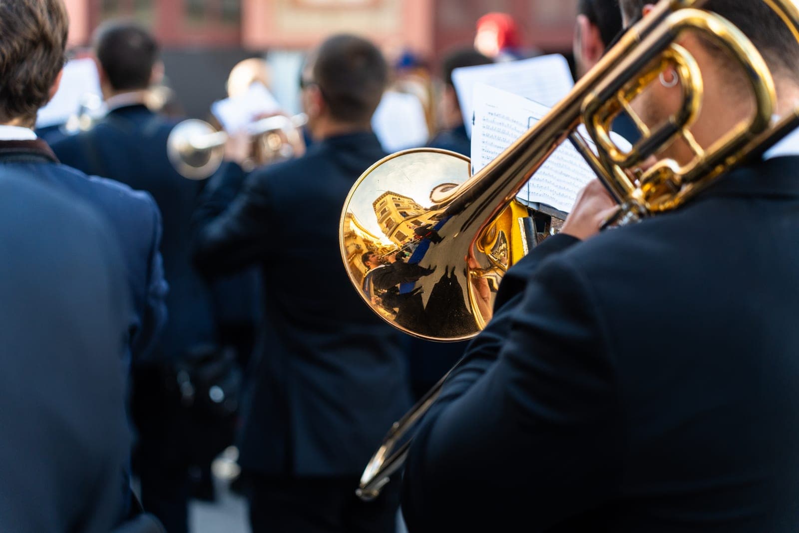 A trombone player in a navy uniform seen from behind, band ranked ahead