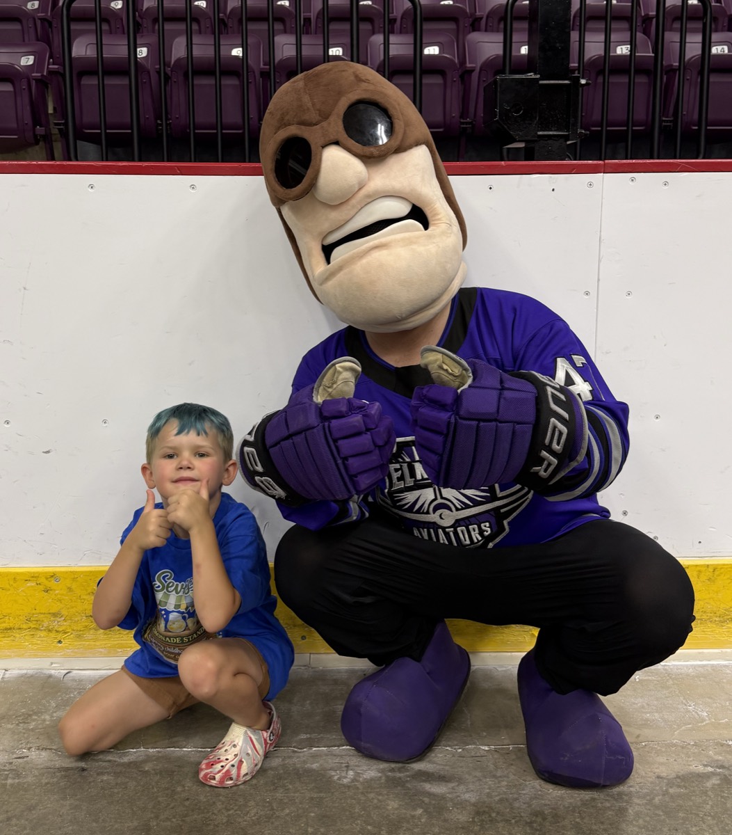 Sevi, in his Sevi's Lemonade Stand shirt, giving a thumbs up beside Ace, the Elmira Aviators mascot, on the arena floor at the LECOM Event Center